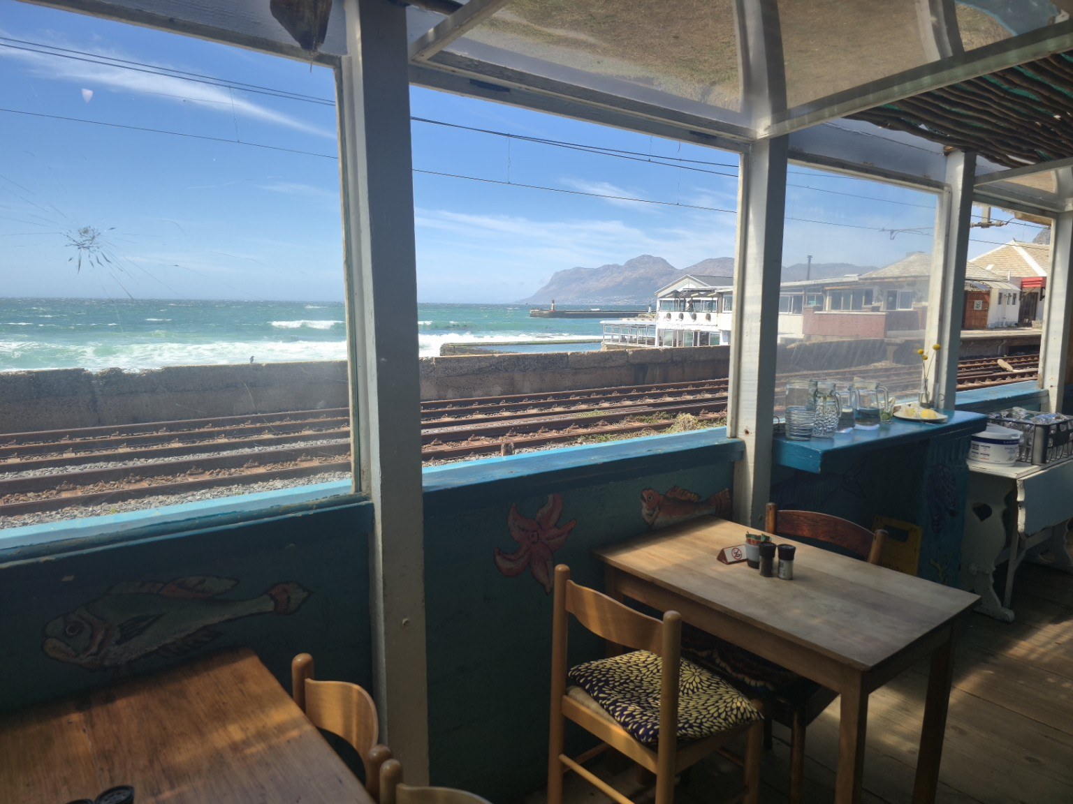 Ocean view from a Kalk Bay harbour restaurant looking across the railway line to False Bay, the harbour breakwater and the mountains beyond, Cape Town