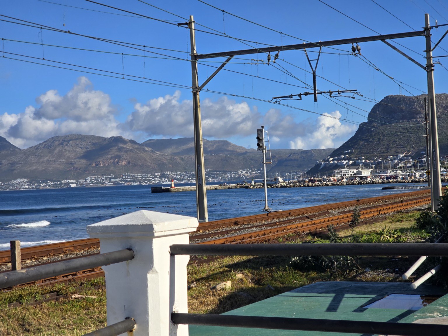 Coastal railway line beside False Bay with Kalk Bay Harbour and mountains in the distance