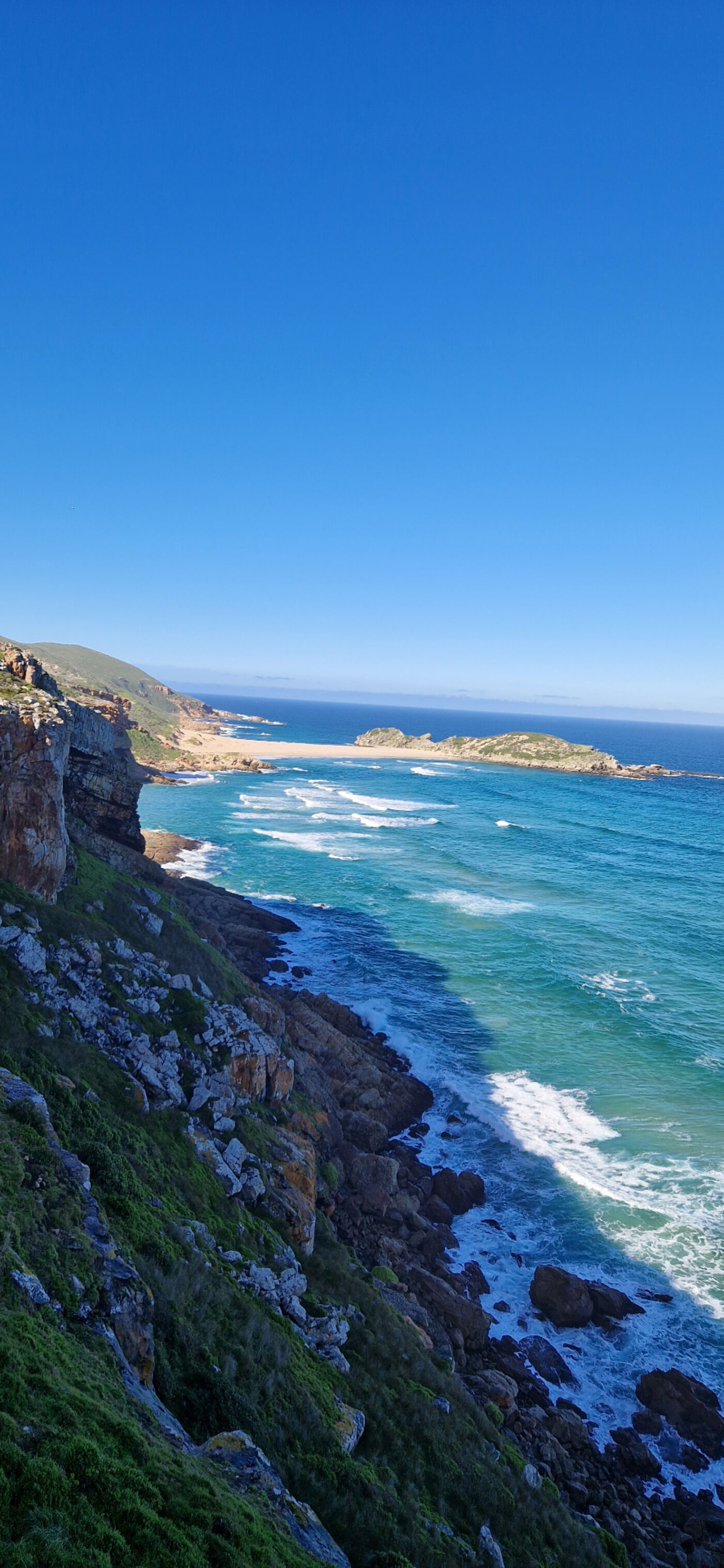 Rugged Robberg Peninsula coastline near Plettenberg Bay — sandstone cliffs, a secluded crescent beach and Robberg Island surrounded by clear turquoise Indian Ocean water