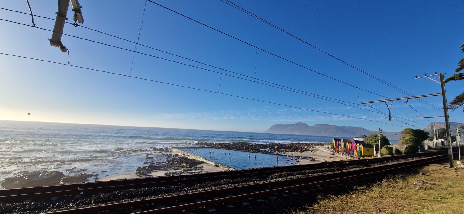 St James tidal pool & railway St James tidal pool beside the Southern Line railway with the colourful bathing boxes and False Bay coastline, Cape Town