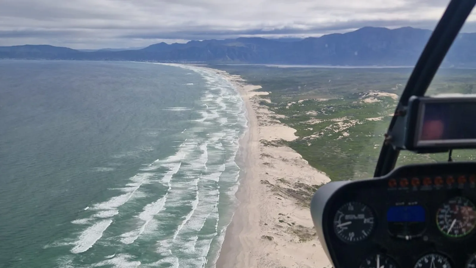 View along the Hermanus coastline and Overberg mountains from the cockpit of a whale watching helicopter